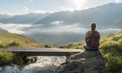 Wanderer sitzt am Steg vor Bergpanorama