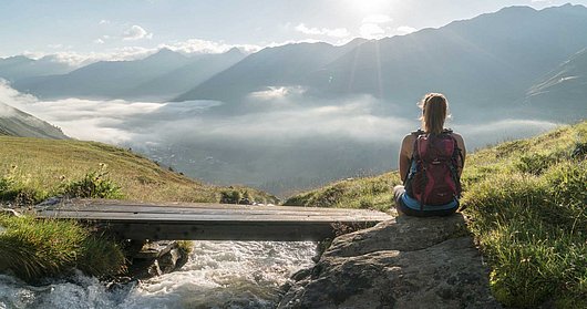 Wanderer sitzt am Steg vor Bergpanorama